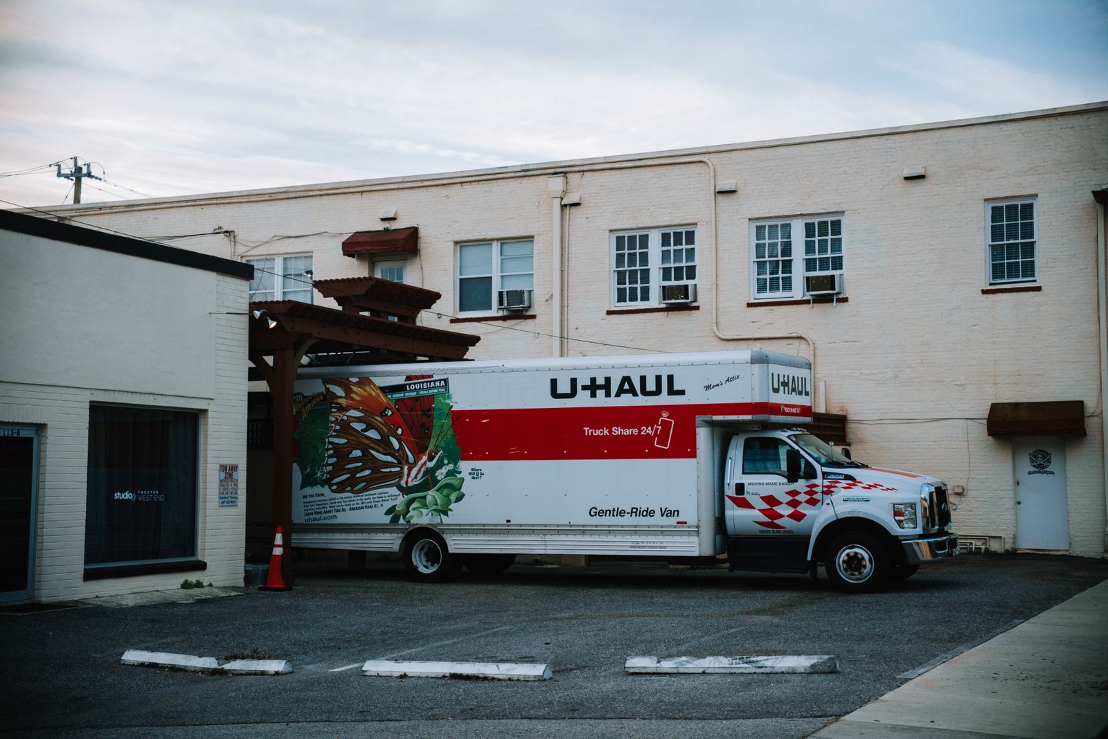 베이지색 벽돌 건물 앞에 주차된 흰색과 빨간색 U-Haul 이사용 트럭