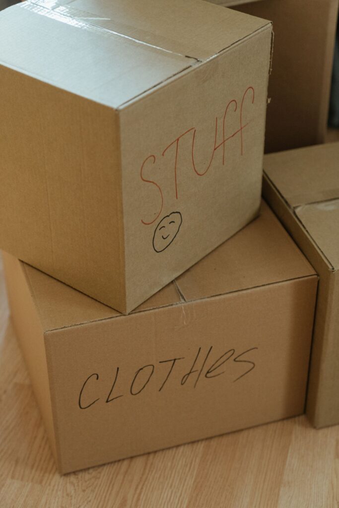 ‘STUFF’와 ‘CLOTHES’라고 적힌 종이 상자들이 나무 바닥에 쌓여 있는 모습